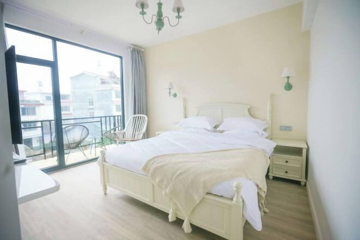 A bedroom with a bed, bedside tables, a chair, and a balcony with a view.