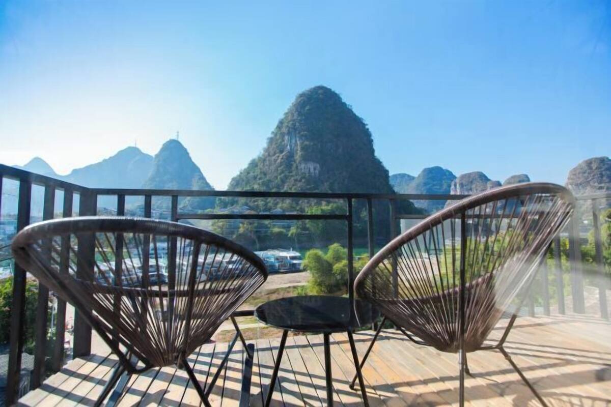 A balcony with two wicker chairs and a small table, overlooking a mountainous landscape.
