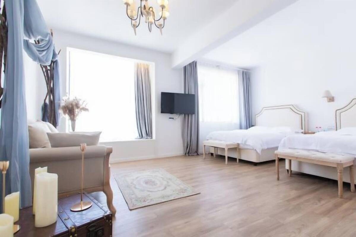 A hotel room with two beds, a sofa, a TV, and a chandelier.