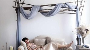 Una persona recostada en un sofá en una habitación con una estructura de ramas y tela colgante.