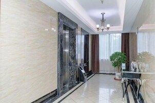 A hotel lobby with a marble wall, a reception desk, a chandelier, and a potted plant.