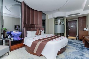 Una habitación de hotel moderna con una cama curvada, un cabecero grande, una mesita de noche y un buró.