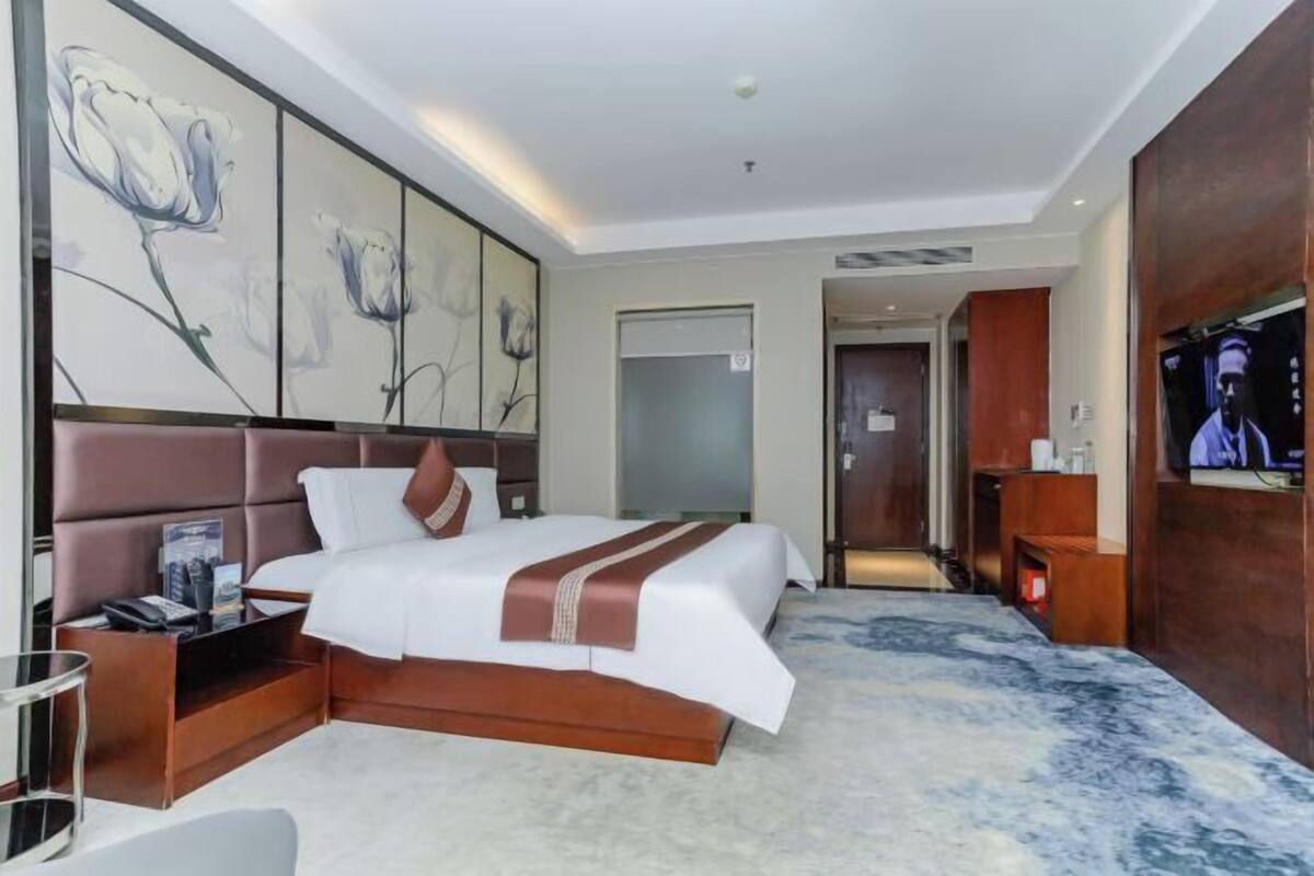 A modern hotel room with a large bed, a flat-screen TV, a desk, and artwork on the wall.
