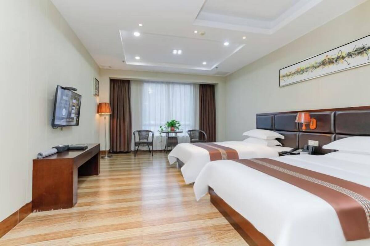 A hotel room with two beds, a desk, a chair, a TV, and a window with curtains.