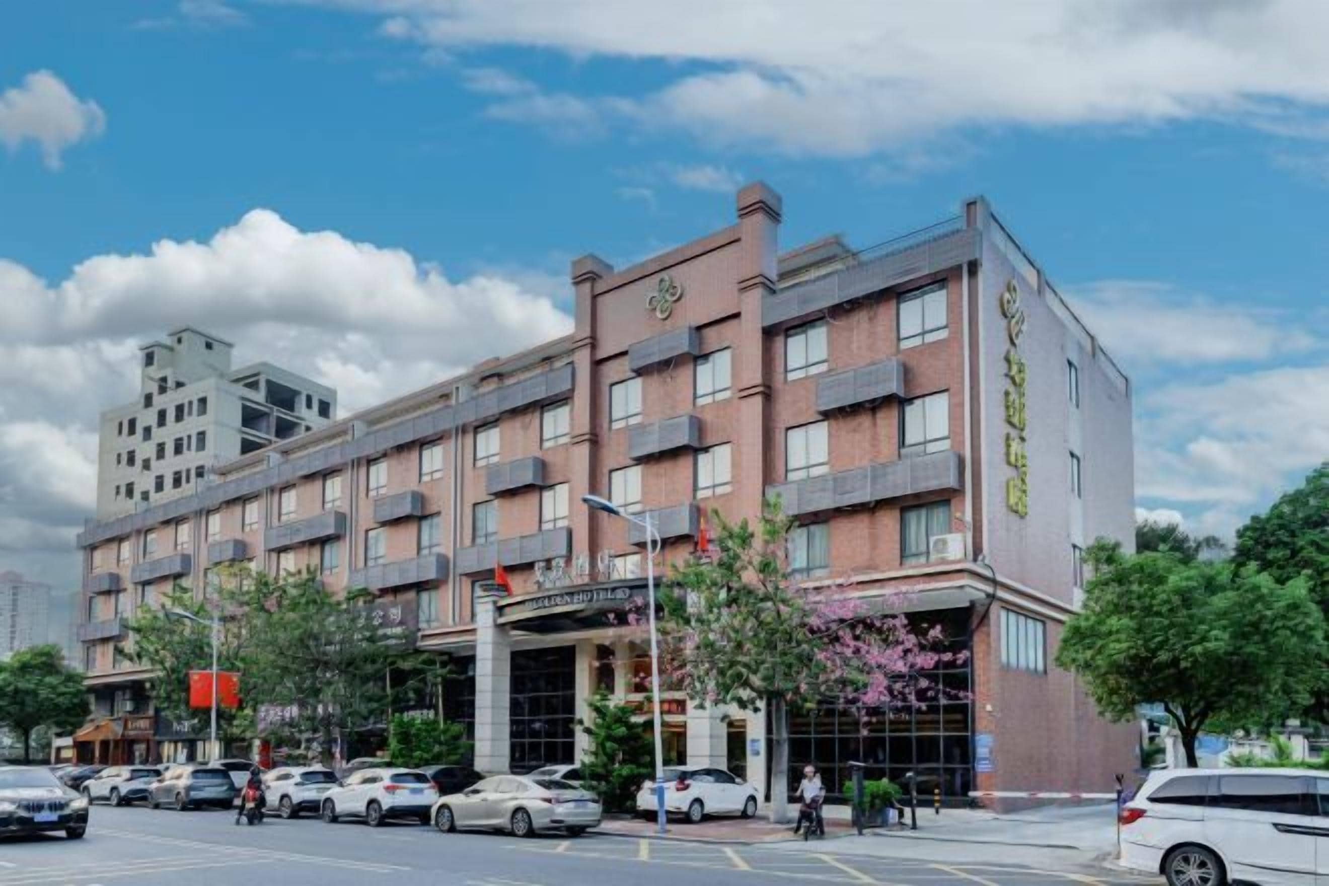 A multi-story hotel with a prominent entrance, several parking spaces, and a clear sky.