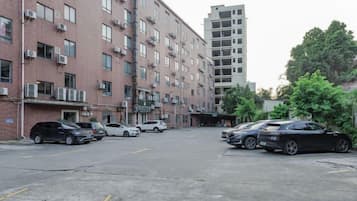 A parking lot with multiple cars, a multi-story brick building with air conditioning units, and a taller building in the background.