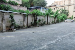 A parking area with a car, a wall with plants, and a building in the background. - Golden Hotel (Sihui)