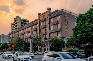Un hotel de varios pisos con fachada de ladrillo, múltiples balcones y un estacionamiento con coches.