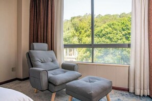 A hotel room with a large window, a grey armchair, and a matching ottoman. - Golden Hotel (Sihui)