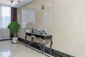 Un hall d’entrée avec un mur en marbre, une plante en pot, une table décorative et un panneau indiquant le numéro de l’étage.
