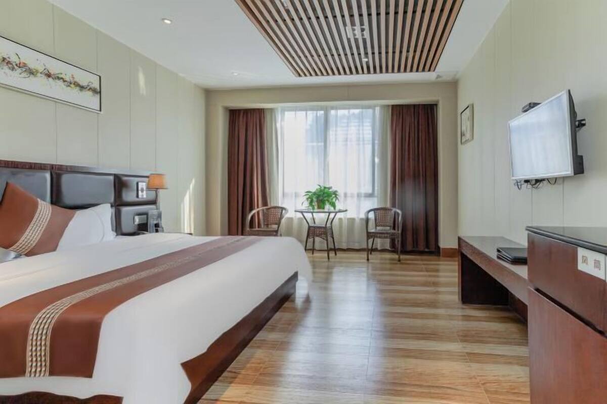 A hotel room with a large bed, a desk, a chair, a TV, and a window with curtains.