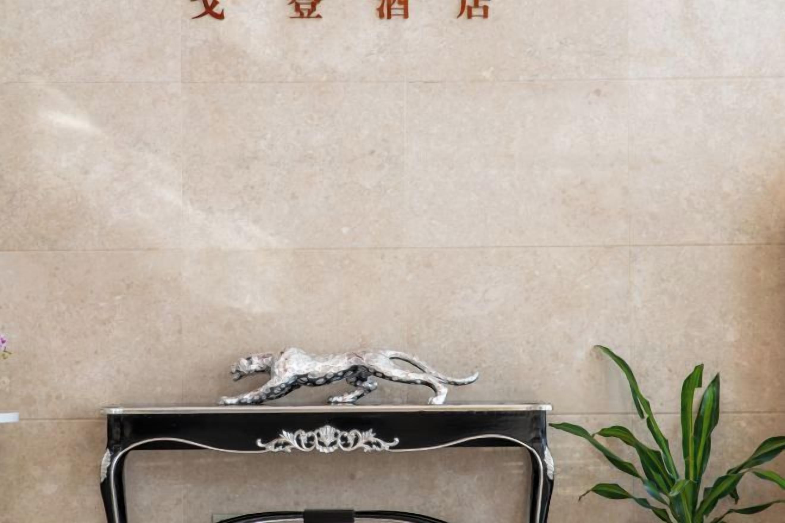 A reception desk with a metallic animal figurine on top, a potted plant to the right, and a wall with text above the desk.