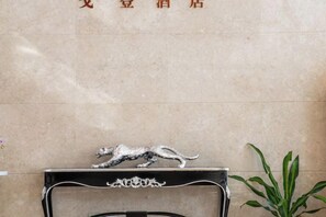 A reception desk with a metallic animal figurine on top, a potted plant to the right, and a wall with text above the desk. - Golden Hotel (Sihui)