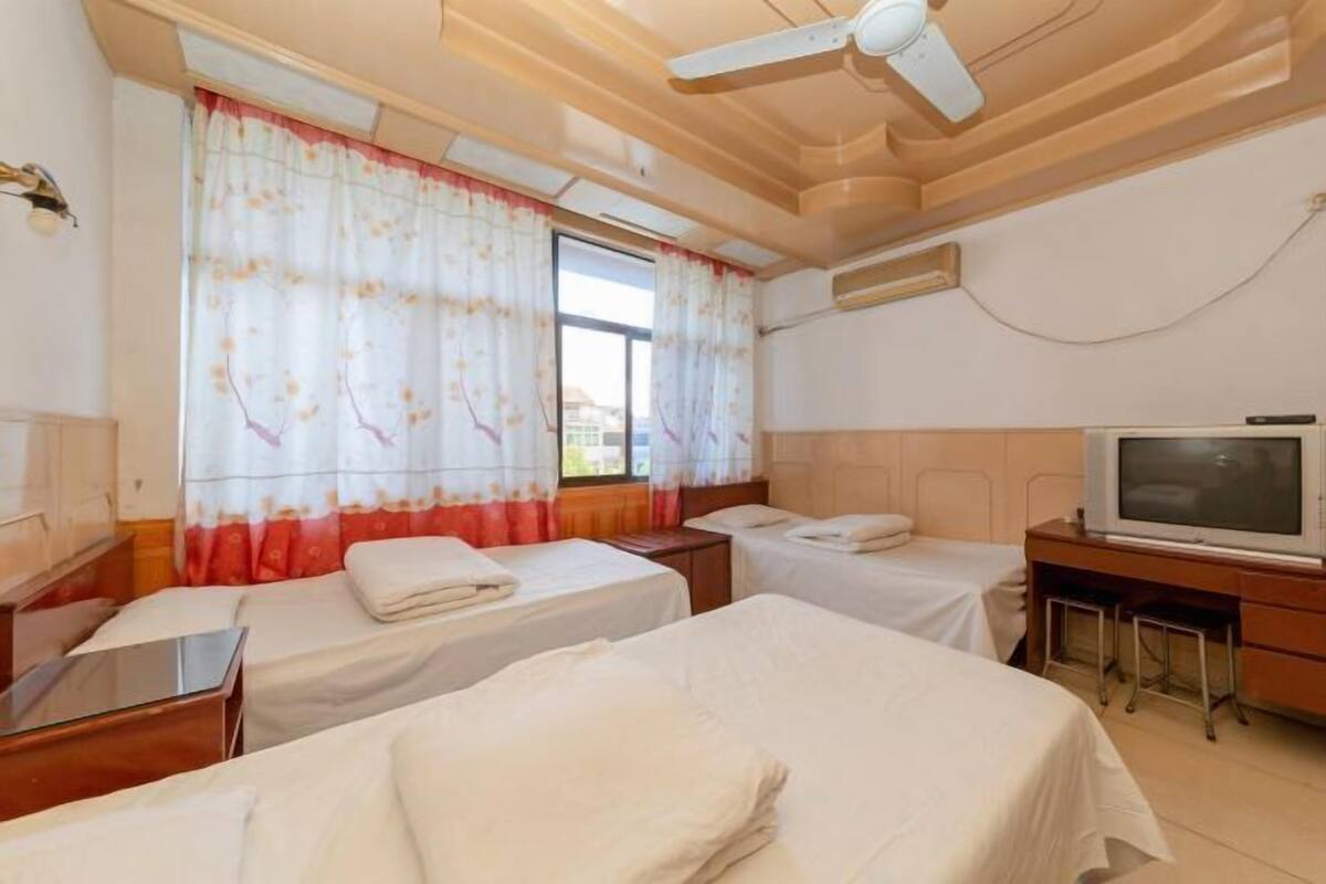 A hotel room with two single beds, a desk with a television, and a ceiling fan.