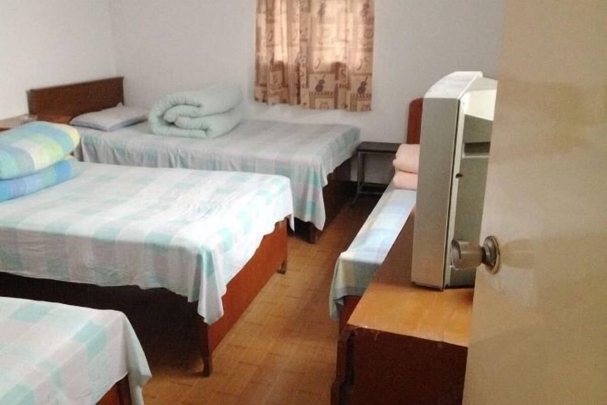 A hotel room with two single beds, a wooden desk, a television, and a window with curtains.