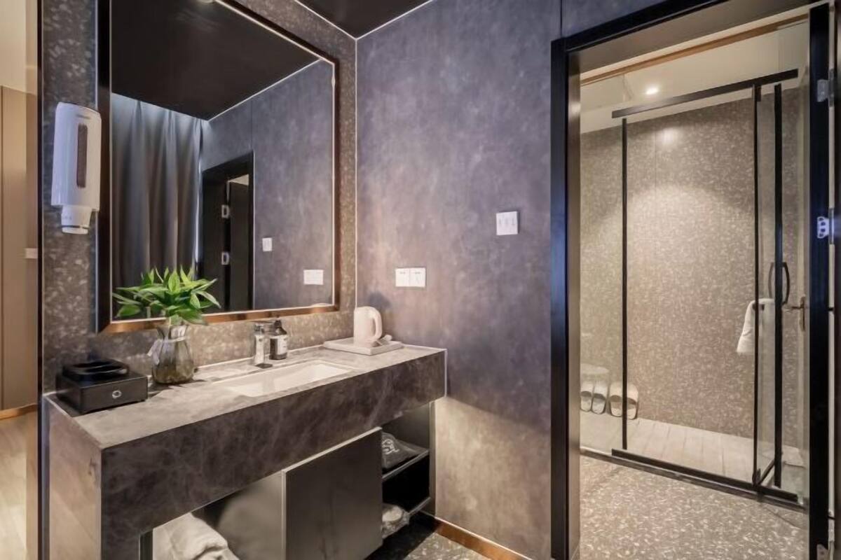 A modern bathroom with a large mirror, a sink, a shower, and a plant.
