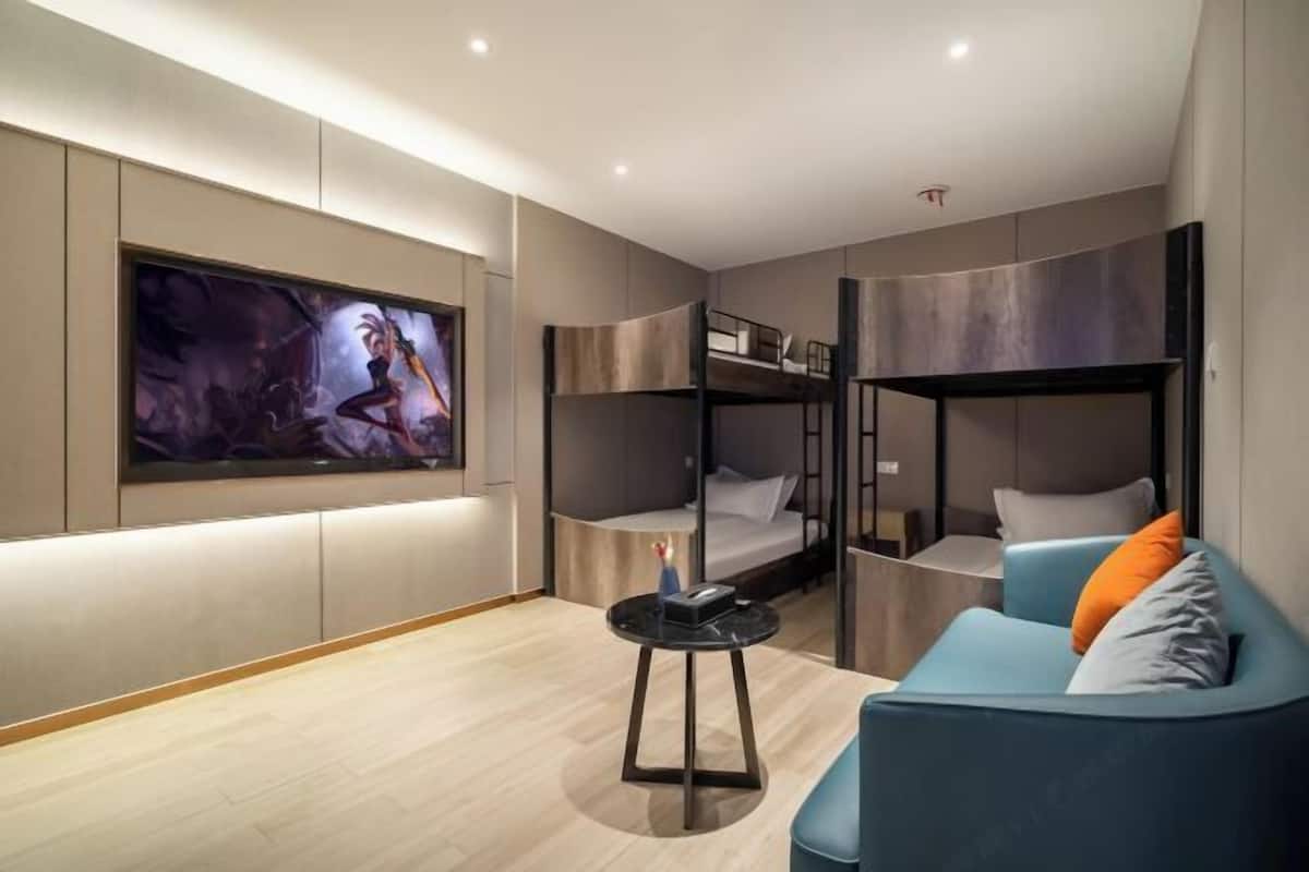 A modern hotel room with bunk beds, a large TV, a sofa, and a small table.