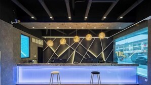 A modern reception area with a geometric wall design, a counter, and two stools. - Danyang Feshang E-sports Hotel (Danyang)