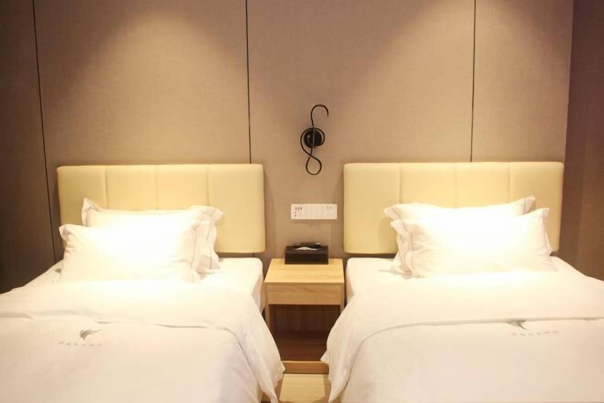 A hotel room with two beds, a nightstand, and a wall-mounted power outlet.