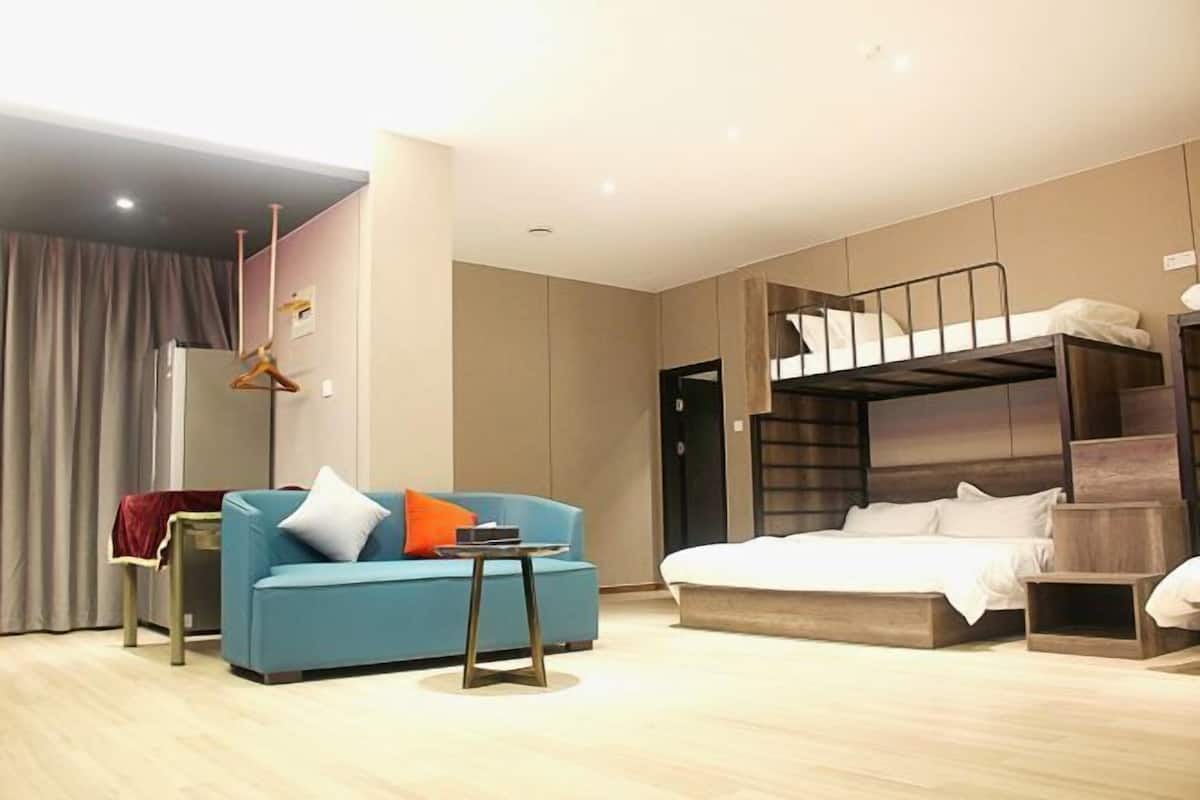 A modern hotel room with a bunk bed, a sofa, a small table, and a curtain.