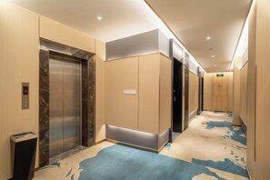 Un pasillo de hotel con ascensores, suelo alfombrado y un aplique en la pared.