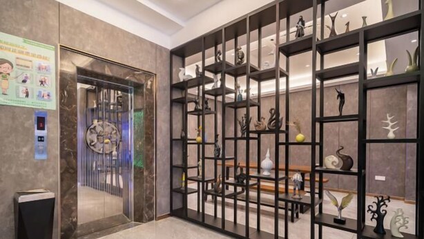A lobby with a marble floor, a glass elevator, and a black shelving unit displaying various sculptures. - Danyang Feshang E-sports Hotel (Danyang)
