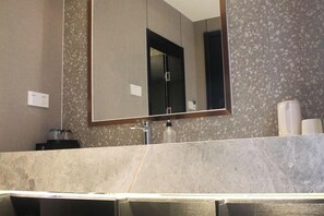 Un bagno con uno specchio grande, un lavandino e un portascopevoli.