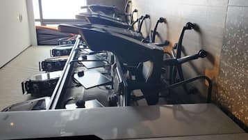 A row of stationary exercise bikes in a room with tiled walls and a window.