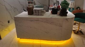 A reception desk with a marble top, a small plant, and a yellow-lit base.