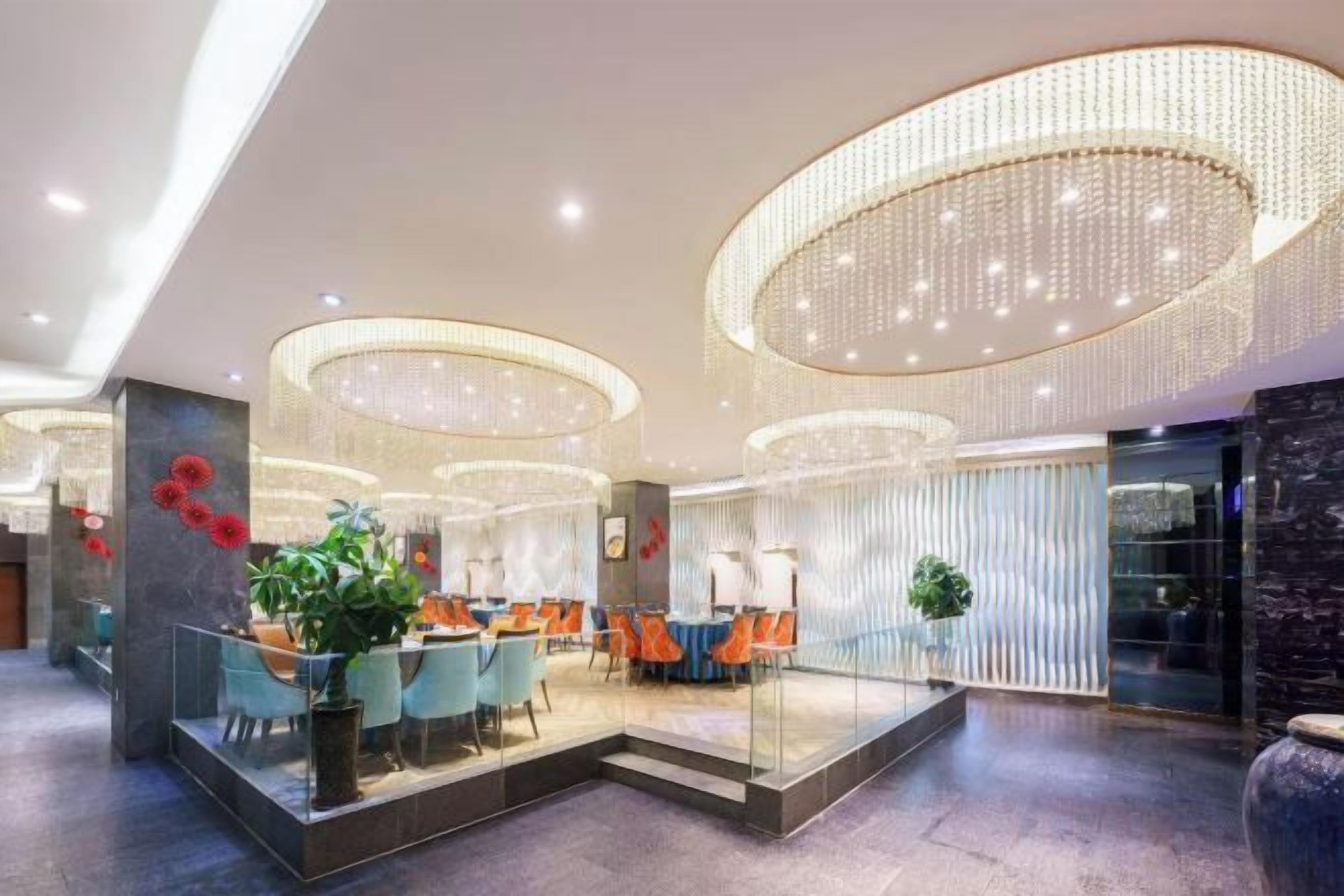 A modern hotel lobby with a central seating area, a reception desk, and a large decorative chandelier.