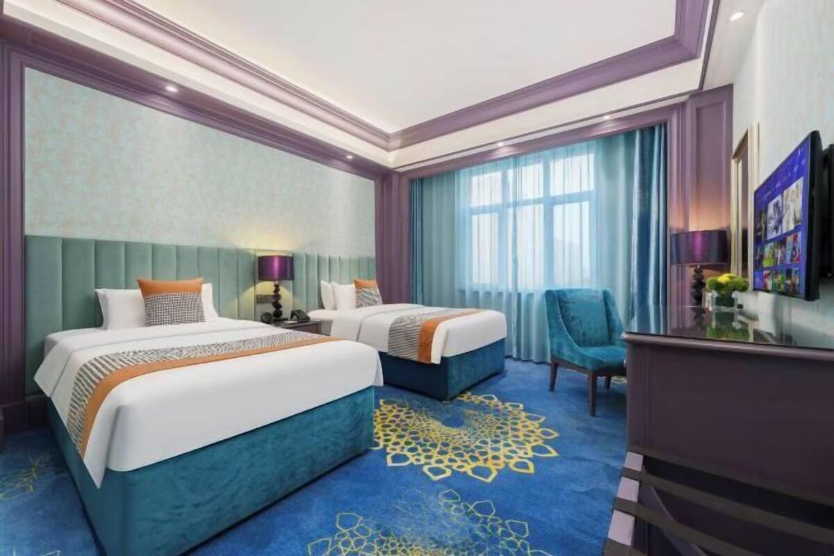 A hotel room with two beds, a desk, a chair, and a large window with curtains.
