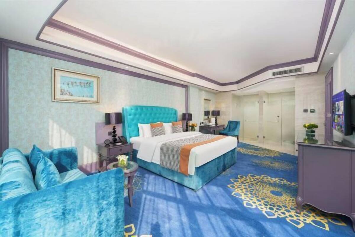A hotel room with a large bed, a sofa, a desk, and a wardrobe.