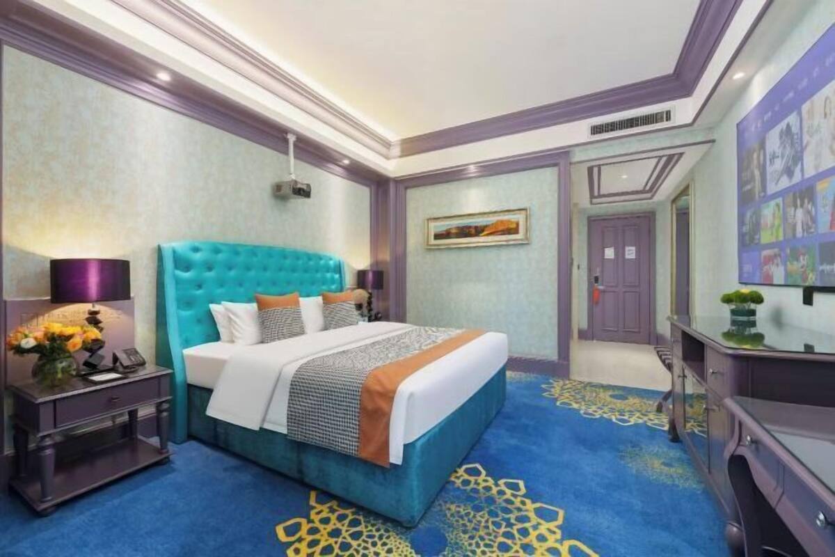A bedroom with a tufted headboard, a large bed with multiple pillows, a nightstand with a lamp, and a dresser.