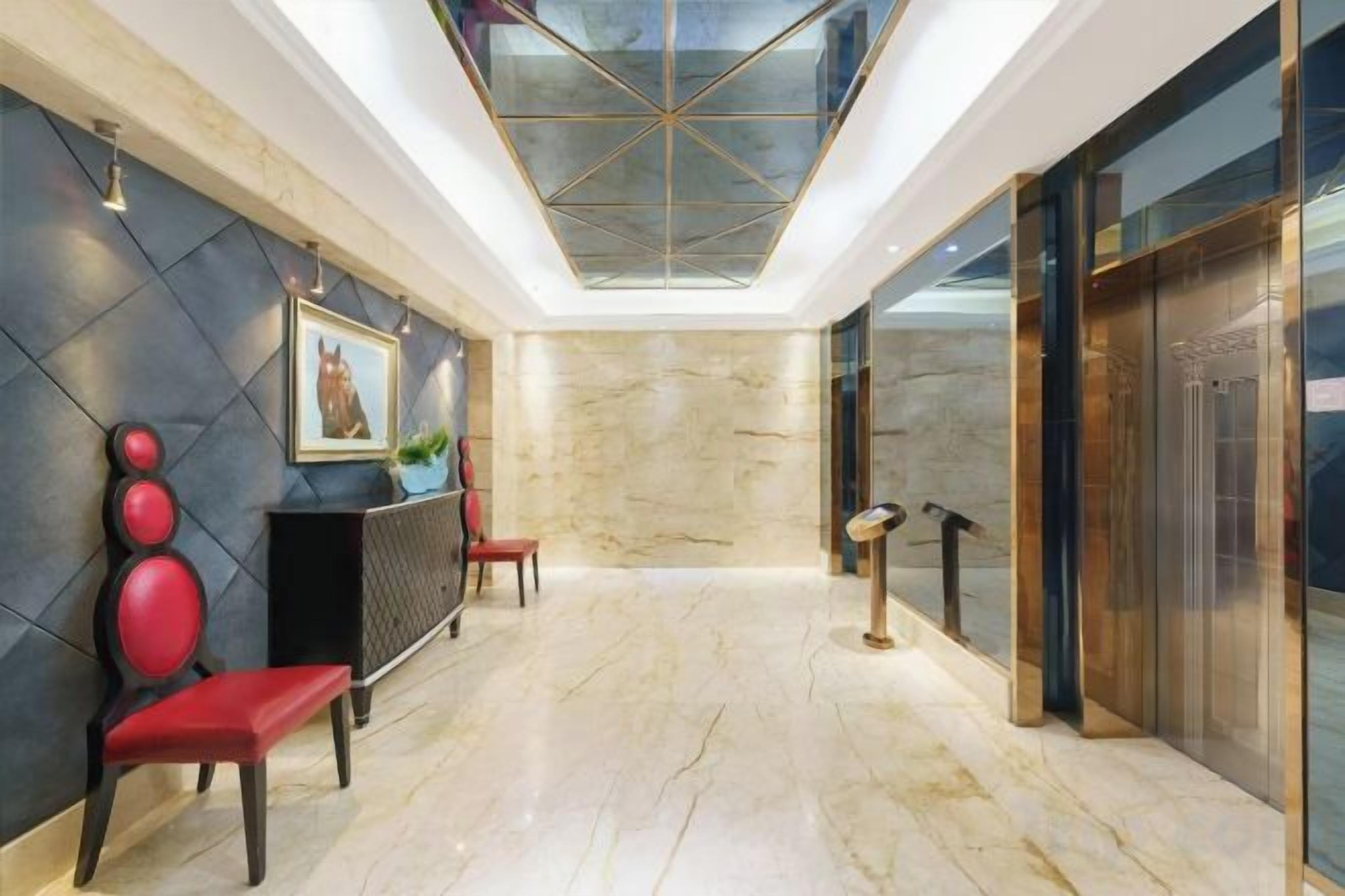 A hotel lobby with a marble floor, a reception desk, red chairs, a painting, and a glass ceiling.