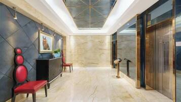 A hotel lobby with a marble floor, a reception desk, red chairs, a painting, and a glass ceiling.