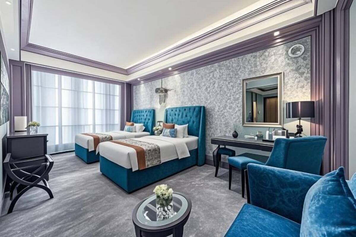 A modern hotel room with two beds, a desk, a chair, and a round coffee table.