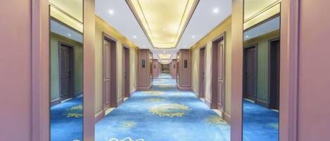 A hotel corridor with mirrored walls, a patterned carpet, and a ceiling light fixture.
