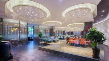 A modern hotel lobby with a central seating area, large chandeliers, and a glass partition.