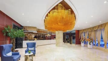 A hotel lobby with a reception desk, seating area, and a large chandelier.