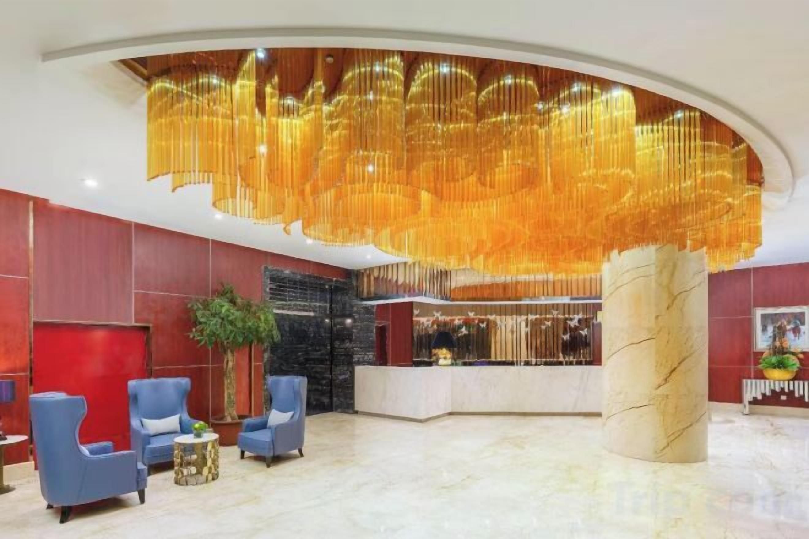 A hotel lobby with a reception desk, seating area, and a large decorative chandelier.