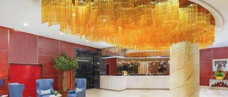 A hotel lobby with a reception desk, seating area, and a large decorative chandelier.