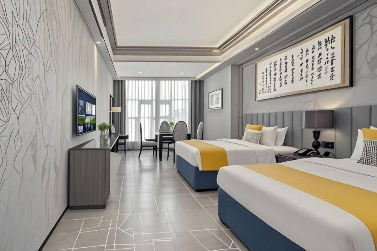 A hotel room with two beds, a desk, a chair, a TV, and artwork on the walls.