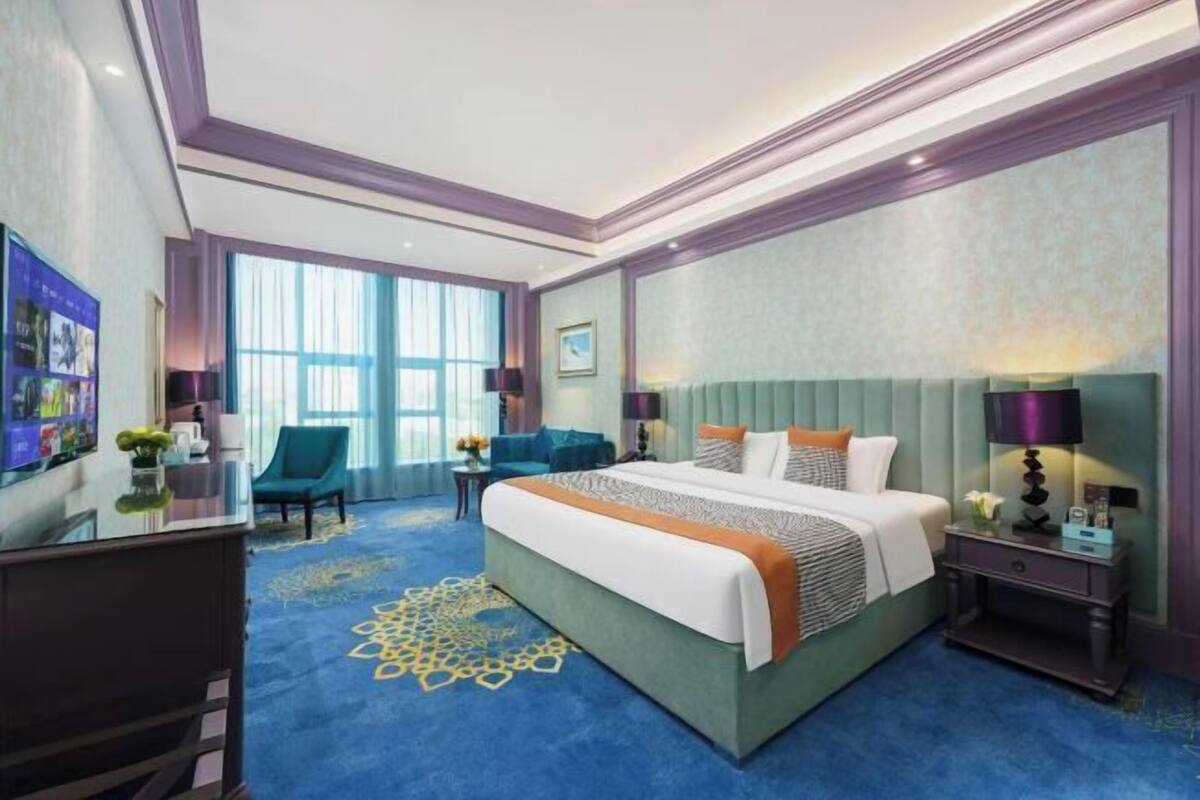 A hotel room with a large bed, a desk, a chair, and a large window.