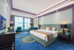 Ein Hotelzimmer mit einem großen Bett, einem Schreibtisch, einem Stuhl und einem großen Fenster.