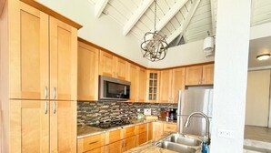 Una cocina con armarios de madera, encimera de granito, electrodomésticos de acero inoxidable y una lámpara colgante.