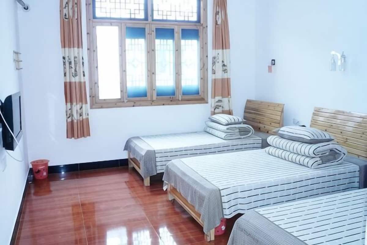 A room with two beds, a wooden headboard, a window with curtains, and a red bucket.