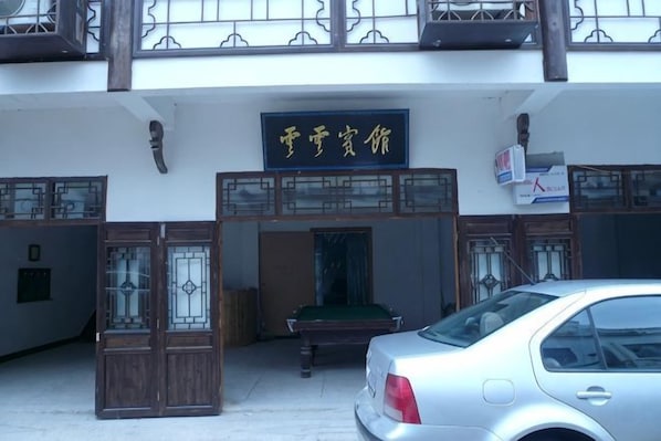 A building entrance with a sign, a car parked in front, and a bench inside. - Yunyun Hotel (Jing County)