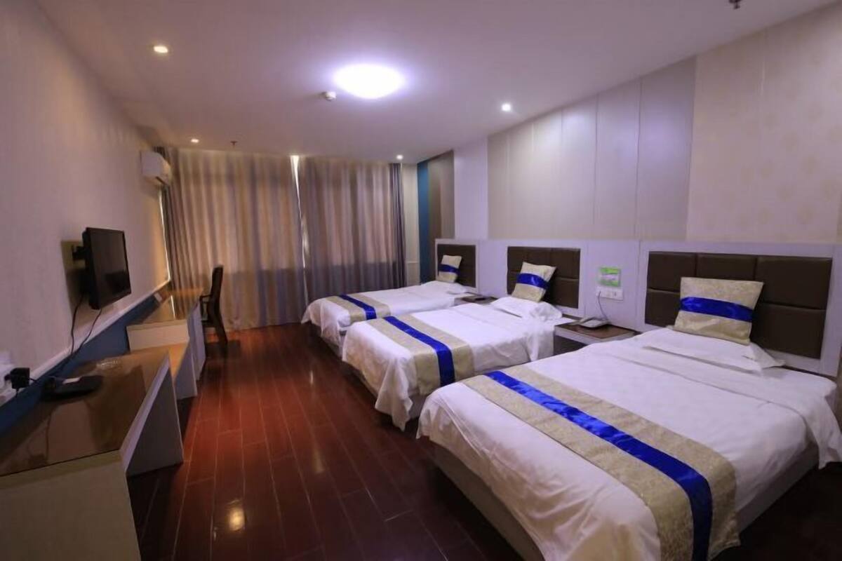 A hotel room with two beds, a desk, a TV, and a window with curtains.