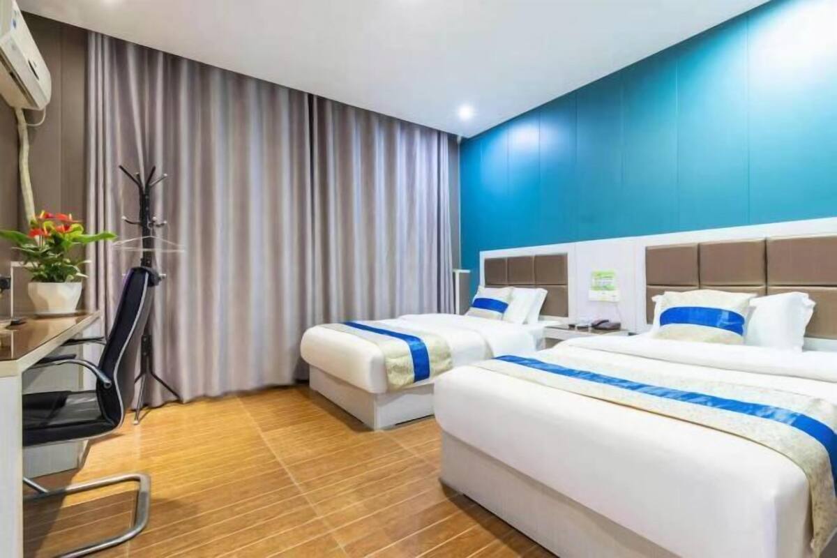 A hotel room with two beds, a desk, a chair, a potted plant, and a curtain.
