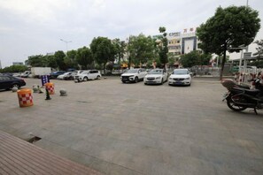 Un estacionamiento con varios coches y una motocicleta, rodeado de árboles y edificios.